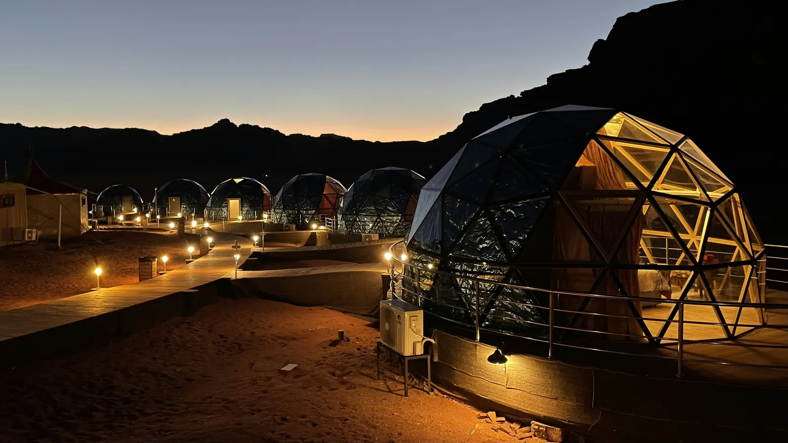 Illustrative: lit geodesic glamping domes at dusk (Wadi Rum, Jordan)