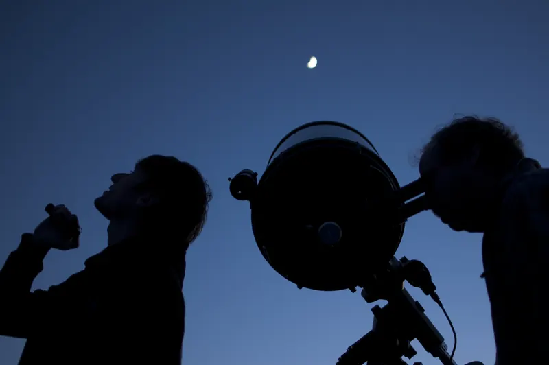 Stargazers and a telescope in silhouette against the blue-hour sky at the Grand Canyon Star Party